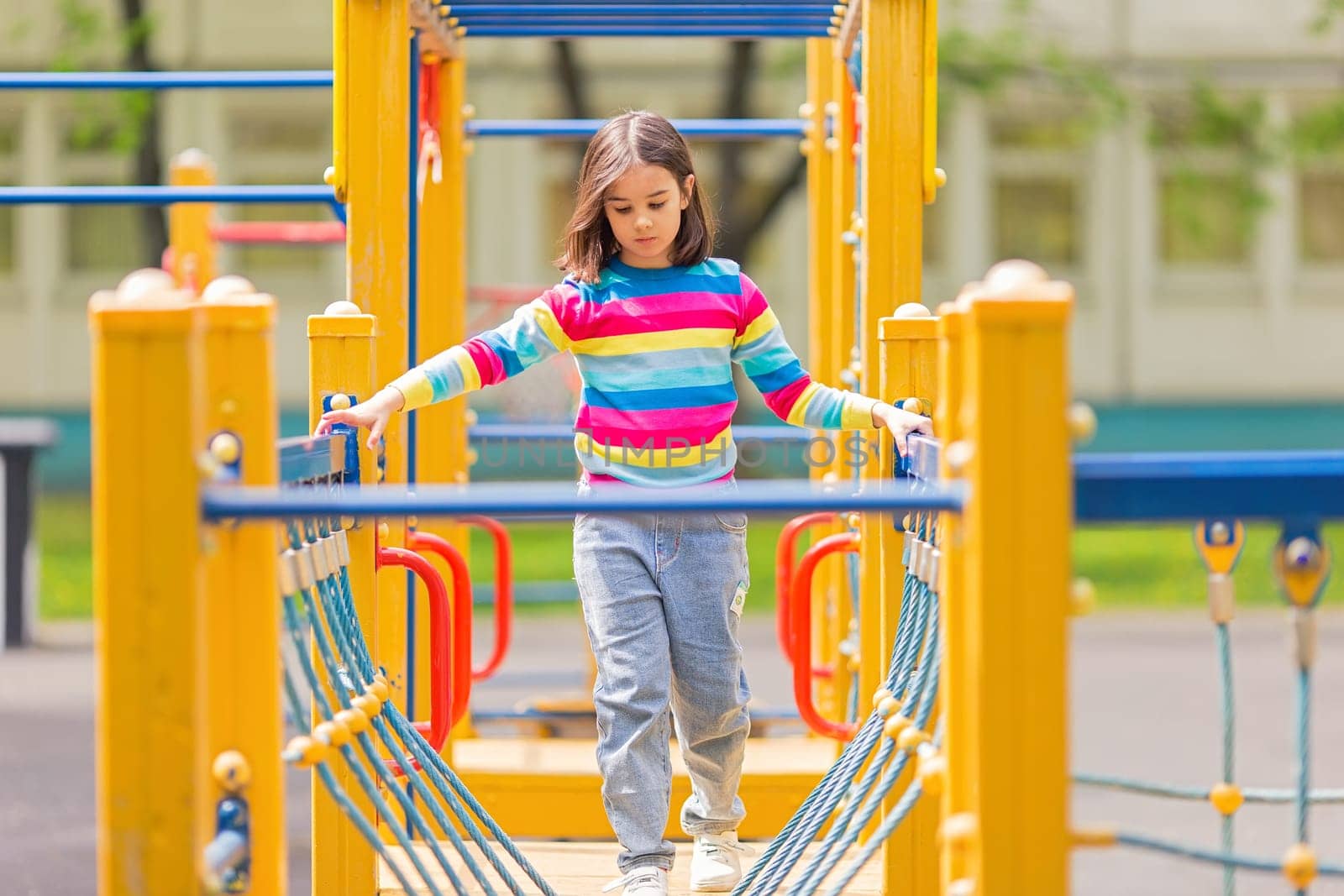 little cute girl 5-6 years on a childrens ladder on a bright yellow playground, in a park, in summer
