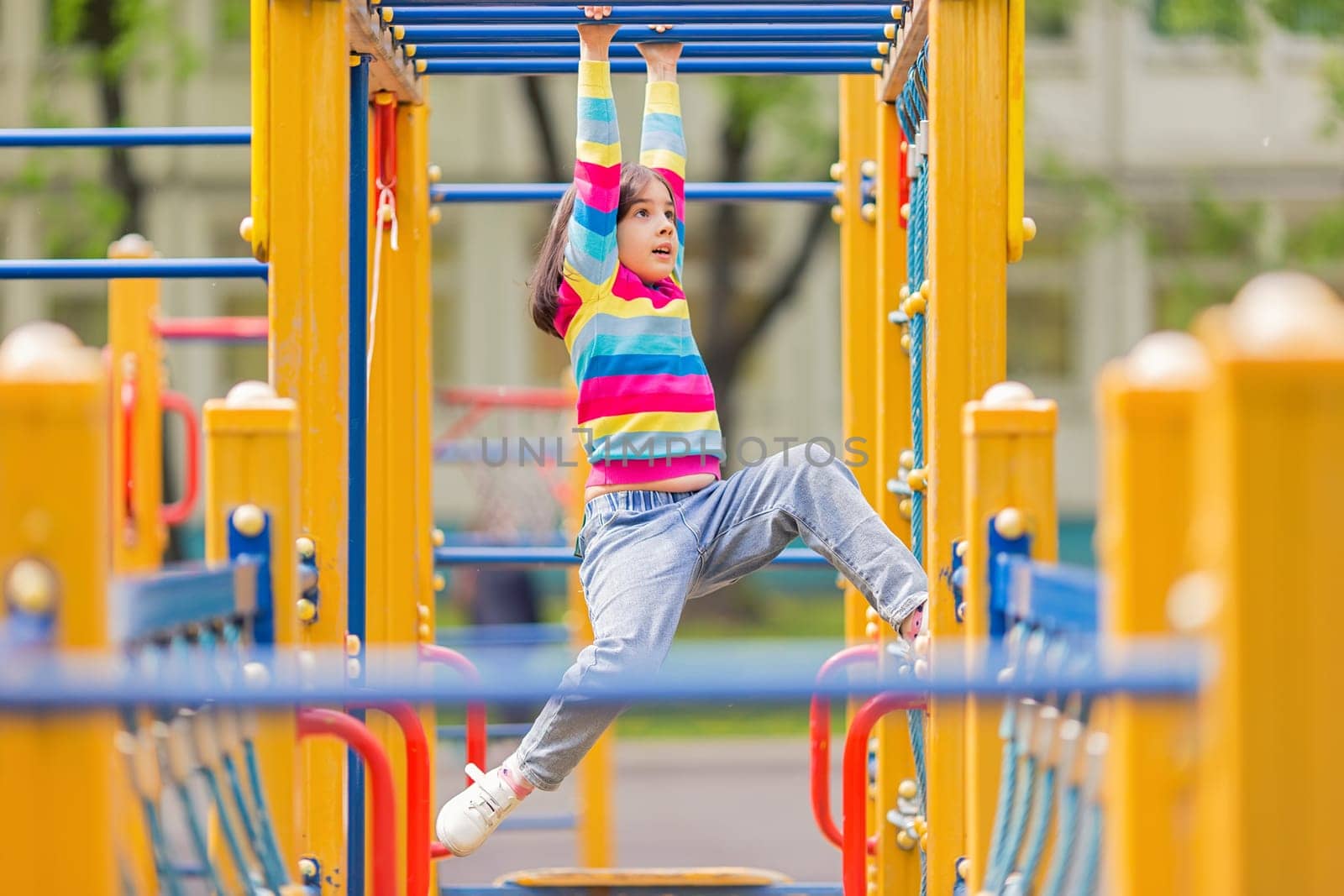 a little 5-6 years old girl hangs on a childrens ladder on a bright playground in the park in summer