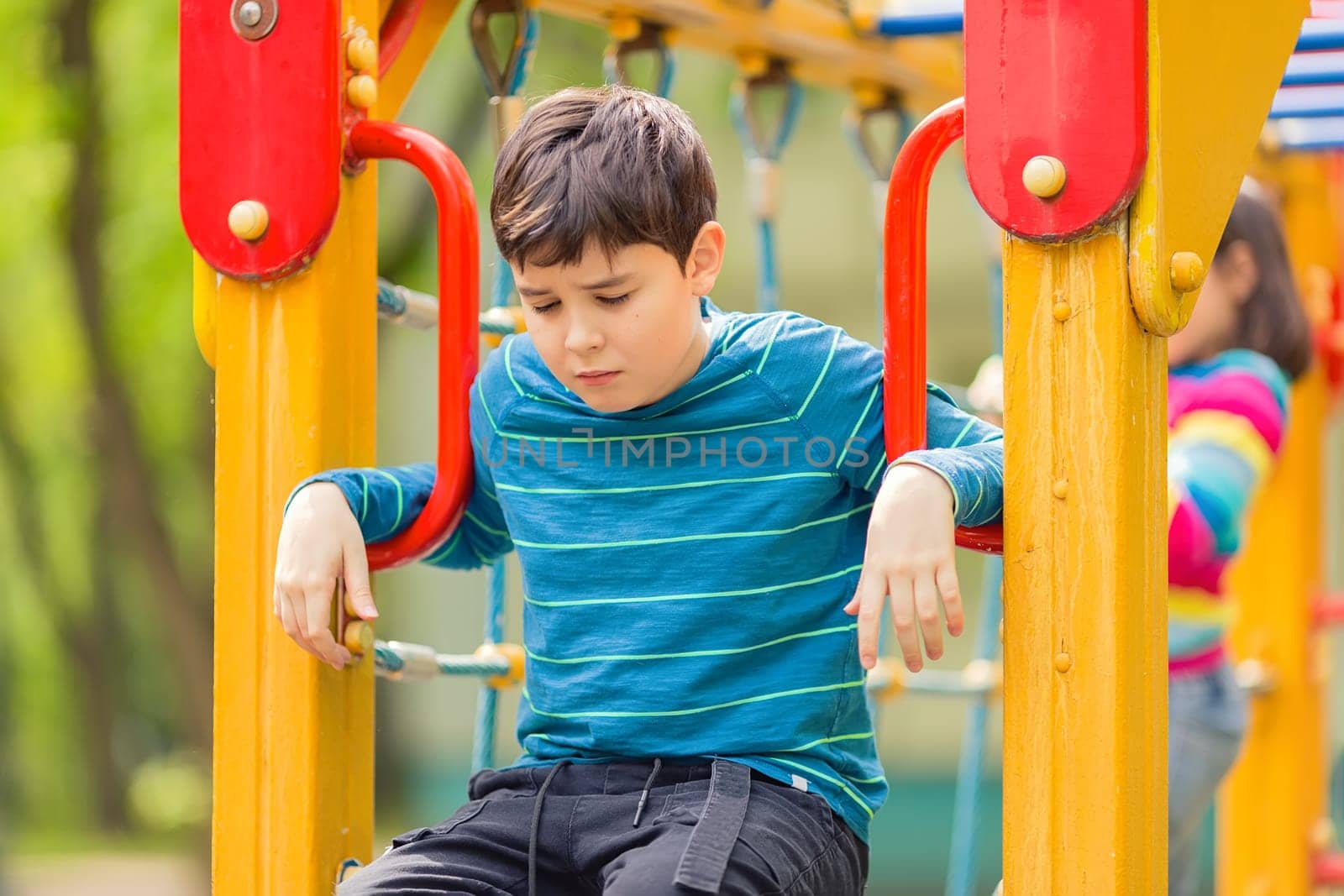 Sad and bored cute teenager sits on a yellow colorful playground in the park, in summer.Close up