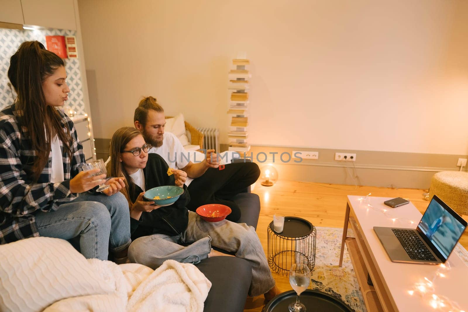 Three close friends gathered in a warm and cozy living room, happily enjoying a movie night filled with snacks