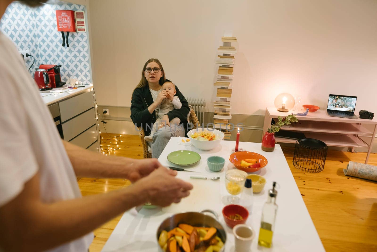A warm and inviting family kitchen scene depicts a loving caregiver gently holding a baby while preparing food