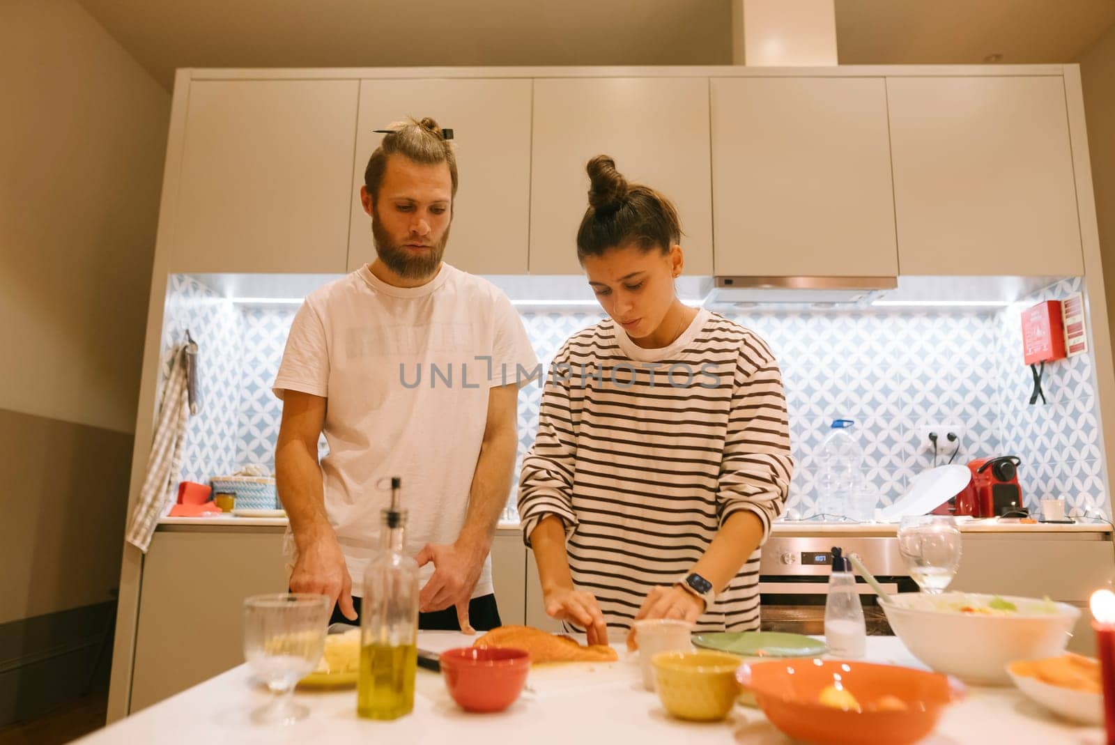 A young couple is joyfully preparing food together in their modern kitchen filled with vibrant, fresh ingredients