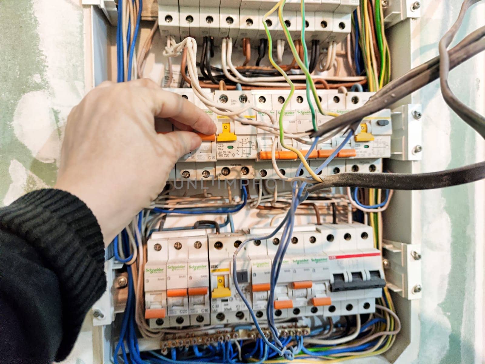 Kirov, Russia - November 26, 2024: Hand is seen working on an electrical switchboard, adjusting wires for proper function and ensuring safety in the system.