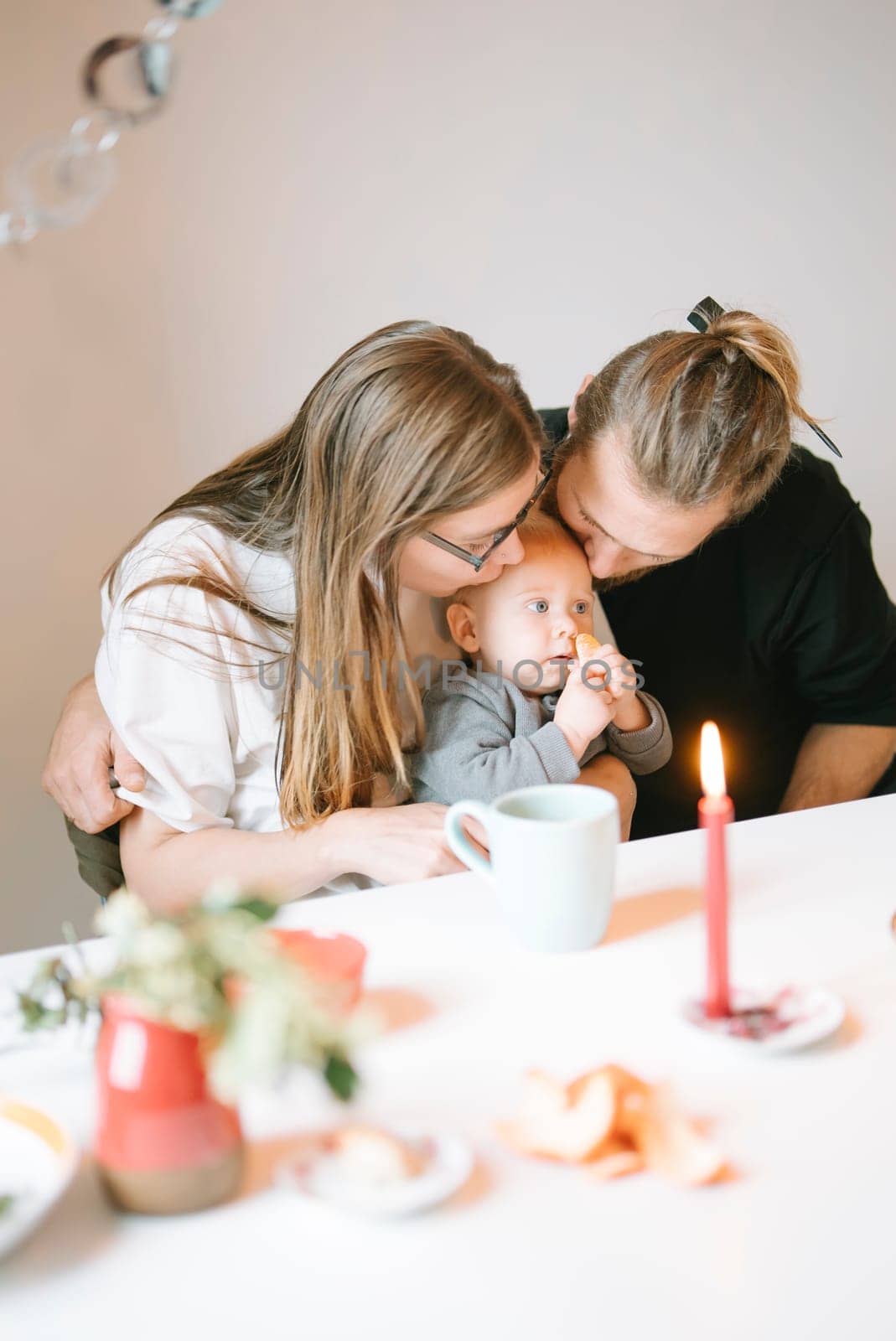 A loving family scene shows parents joyfully sharing a moment with their baby at a cozy table setting