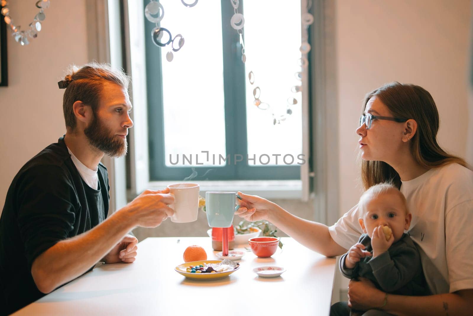 A family happily enjoys a delightful bonding moment together over coffee while lovingly caring for their baby