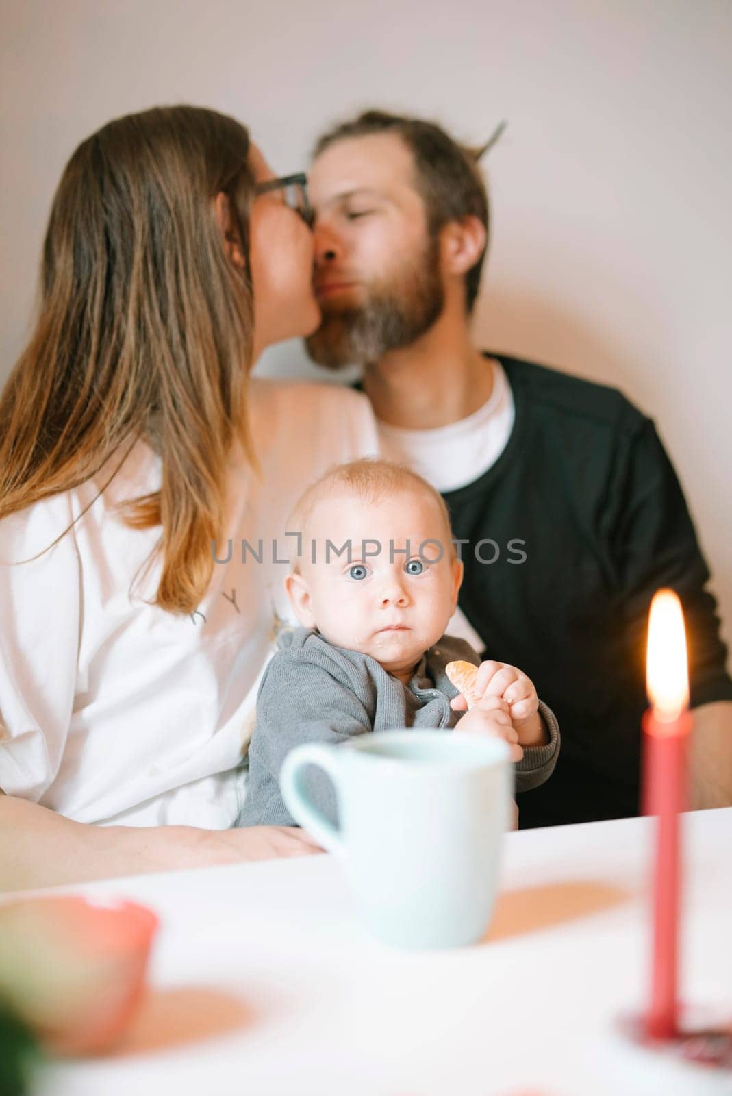 In a tender moment, loving parents share a gentle kiss while cradling their baby in soothing candlelight