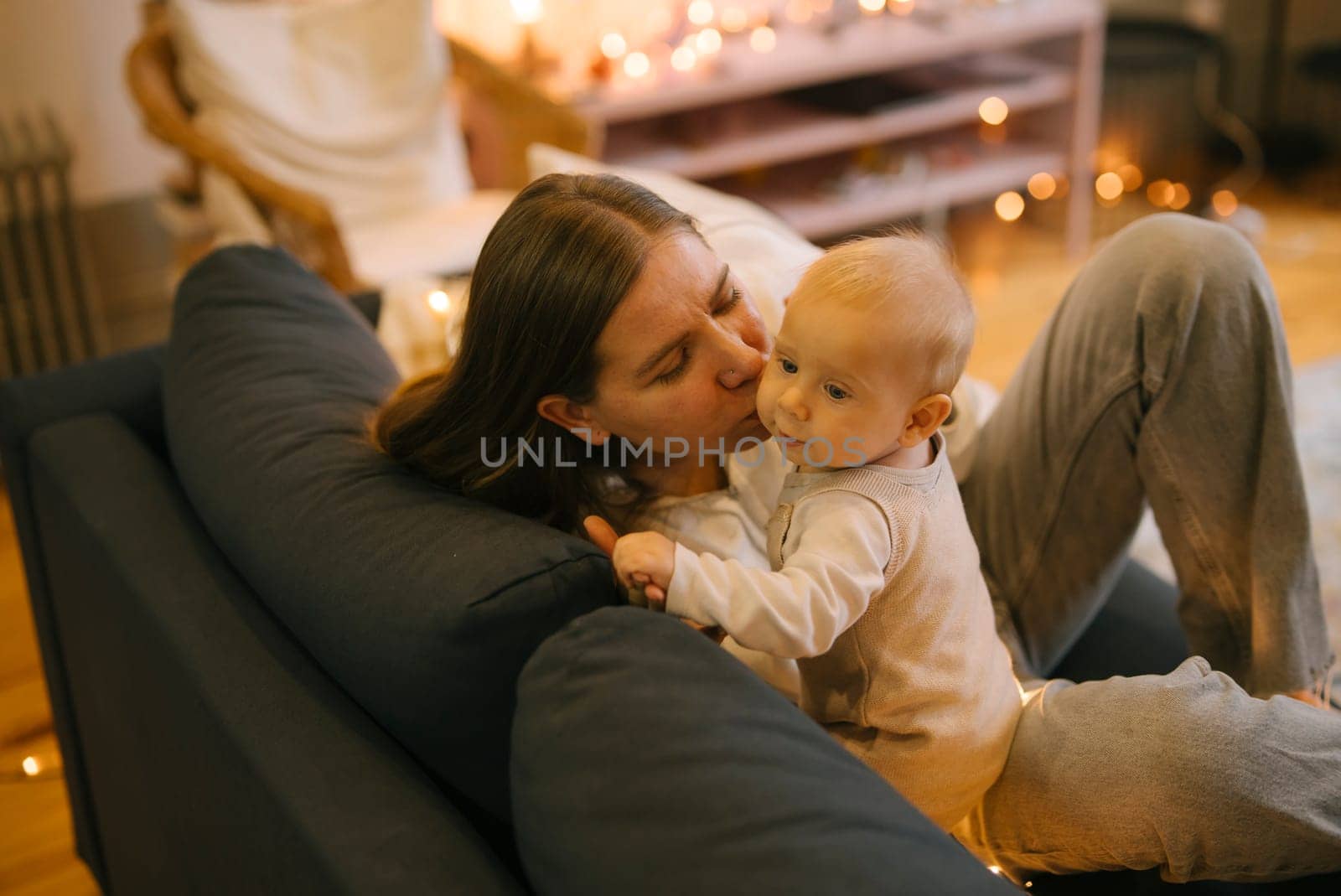A loving mother tenderly kisses her adorable baby while sitting on a cozy couch, enveloped by warm, soothing lights