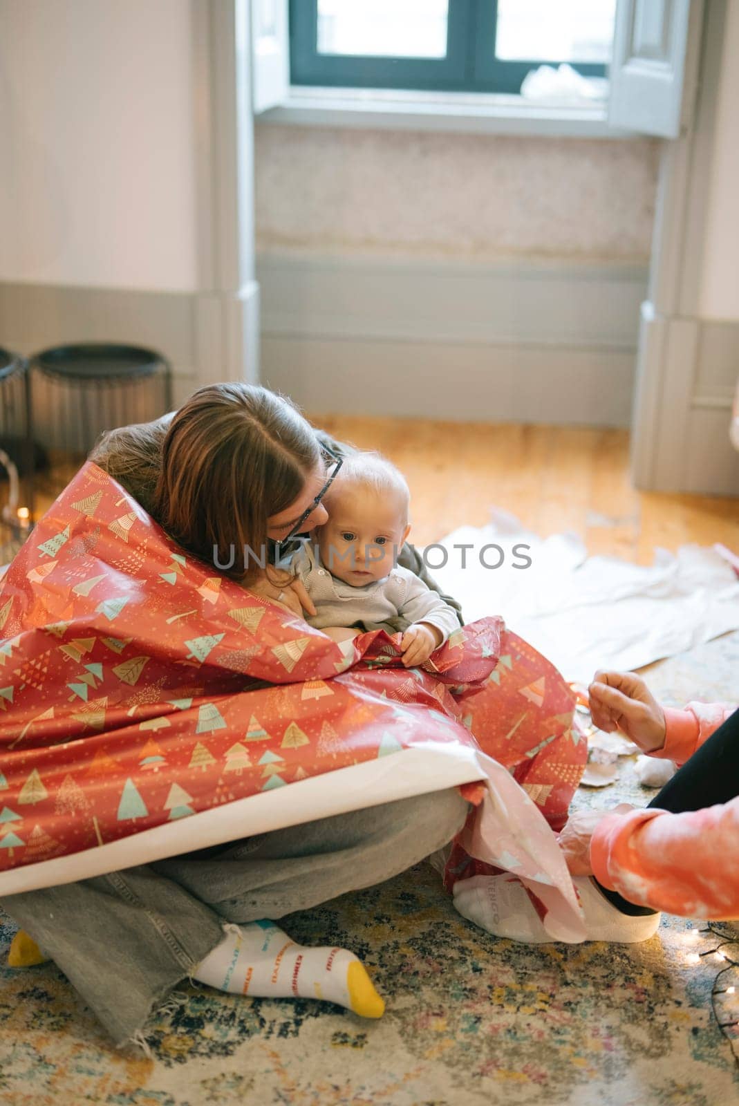 A joyful scene of a loving parent and their baby wrapped in colorful festive paper during the holidays