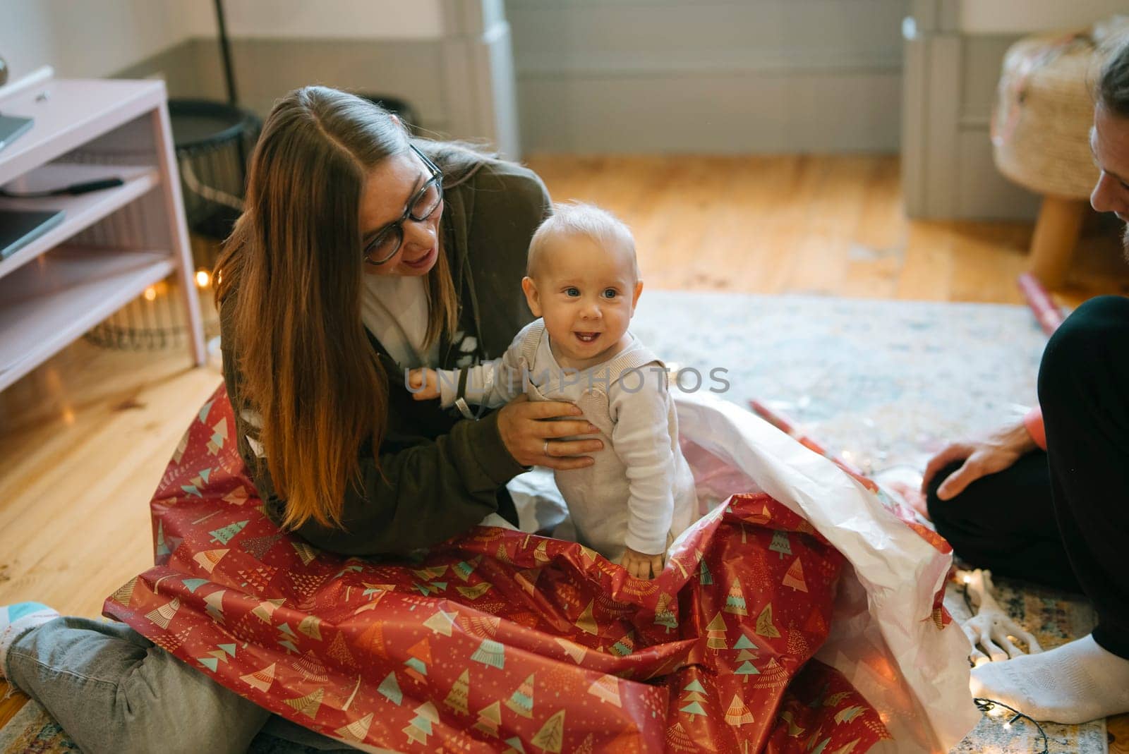 A cheerful little baby happily enjoys playing in colorful gift wrapping during a joyful festive gathering