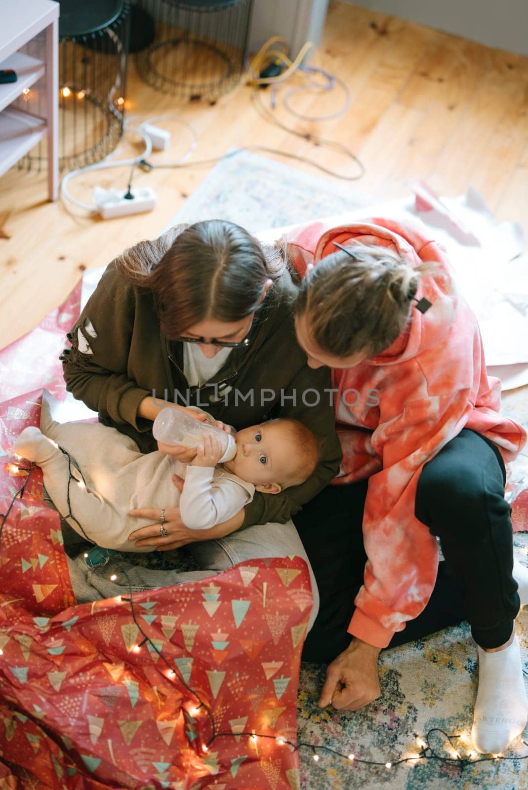 A heartwarming scene of two caring adults interact lovingly with a baby while sitting on a cozy, soft rug