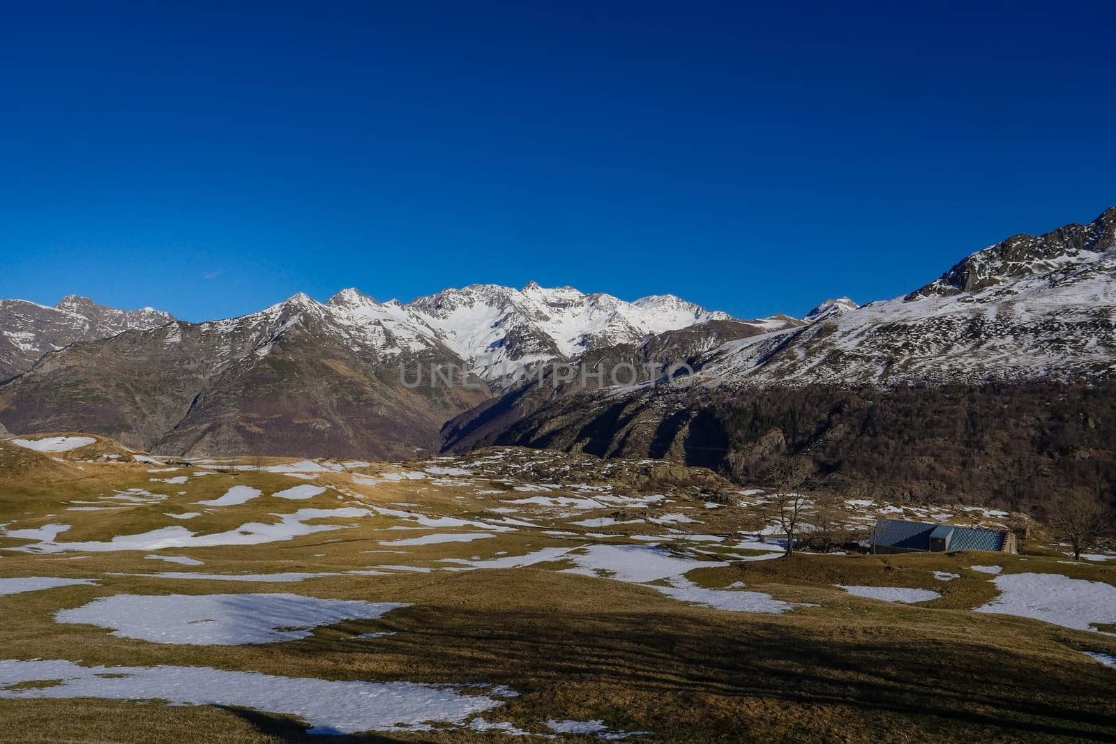 Snow rests on the ground beneath towering mountains, creating a peaceful winter landscape. Bright blue skies enhance the tranquility of this remote location.