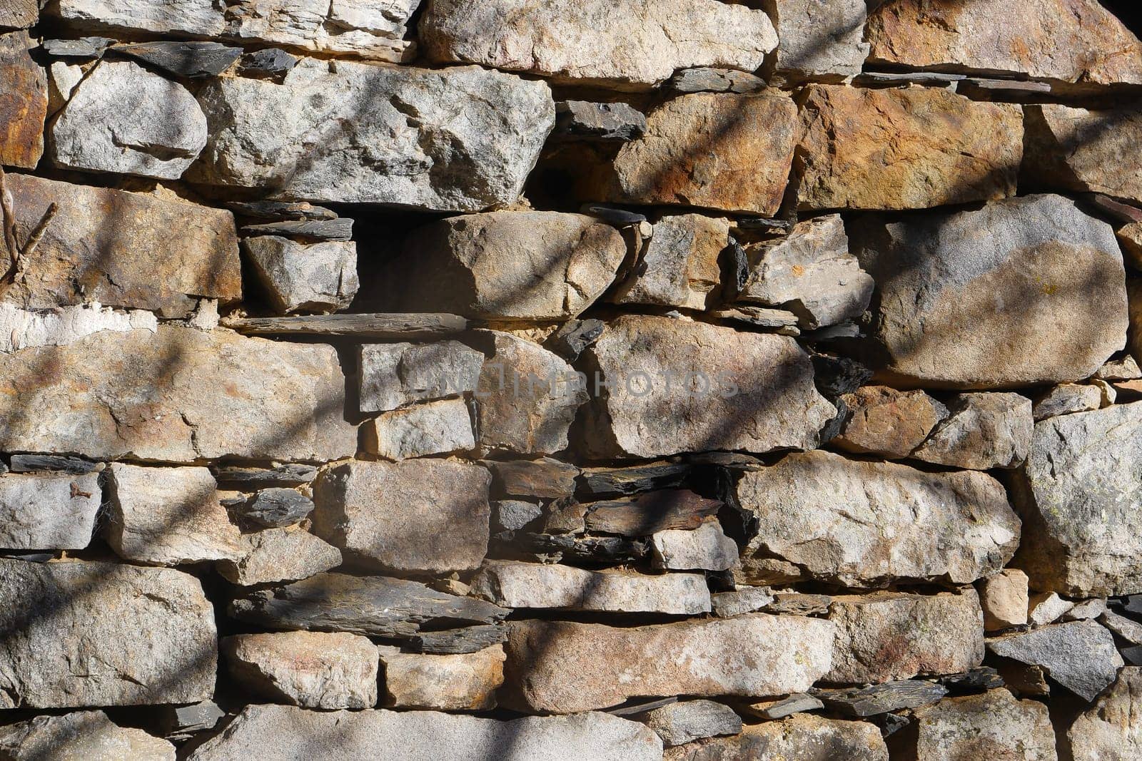 Weathered stones form a sturdy wall, each rock unique in shape and color. The sunlight casts shadows, highlighting the textures. This structure blends harmoniously with the environment.