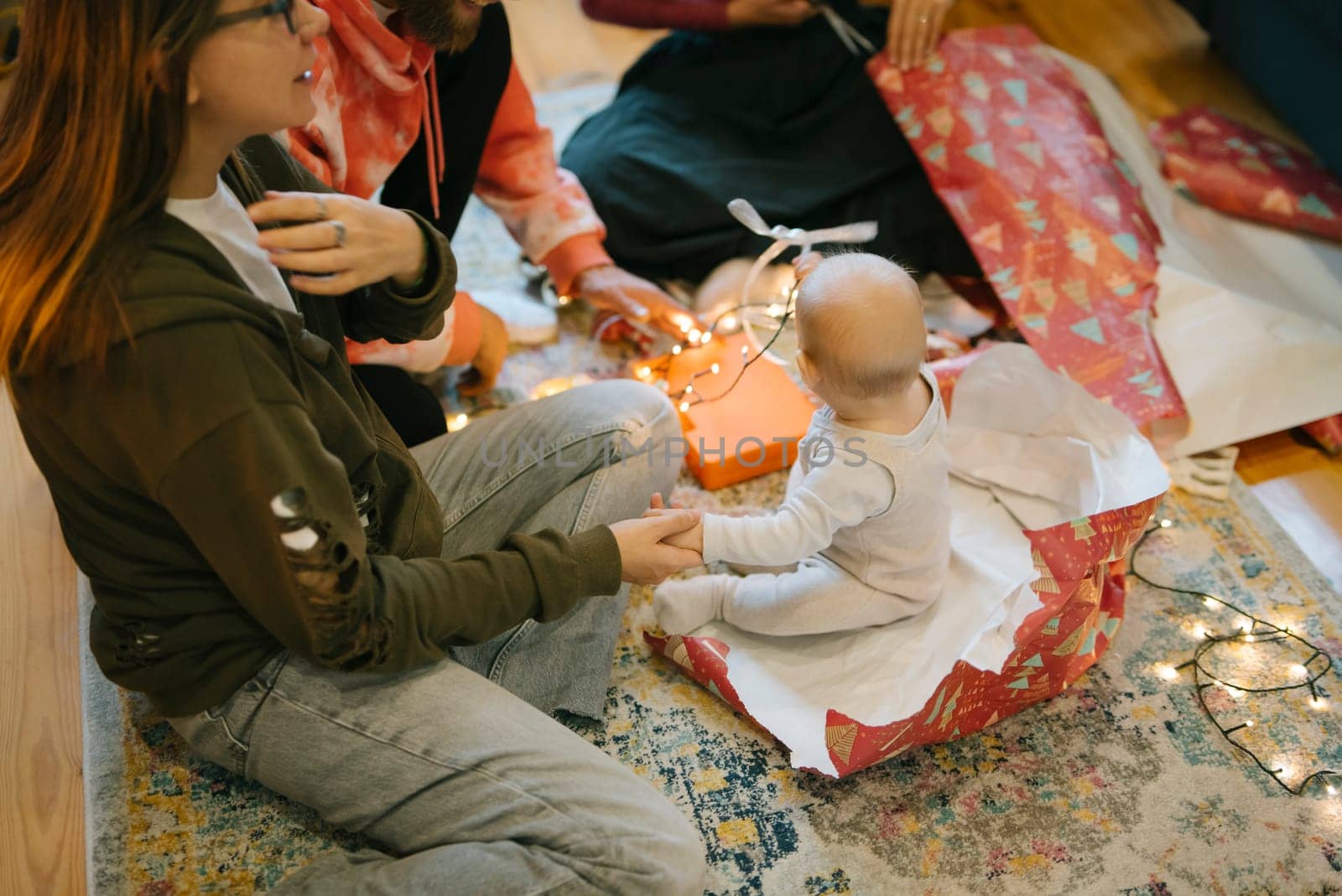 A heartwarming scene depicts a joyful family unwrapping gifts with a cheerful baby surrounded by festive holiday lights