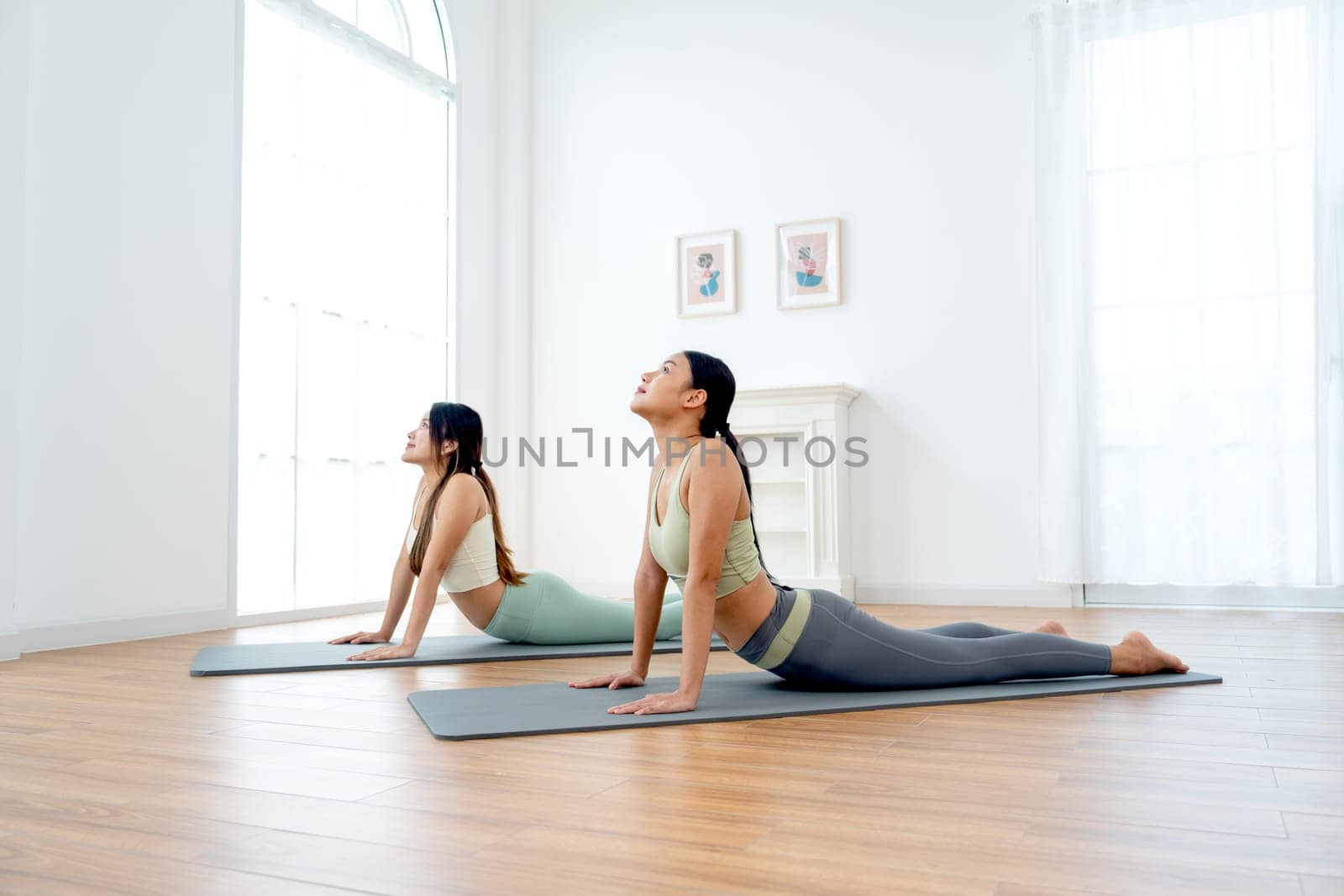 Wide shot of pretty Asian women exercise together with yoga posture by lie down and raise head up also stay on mat in room with day light.