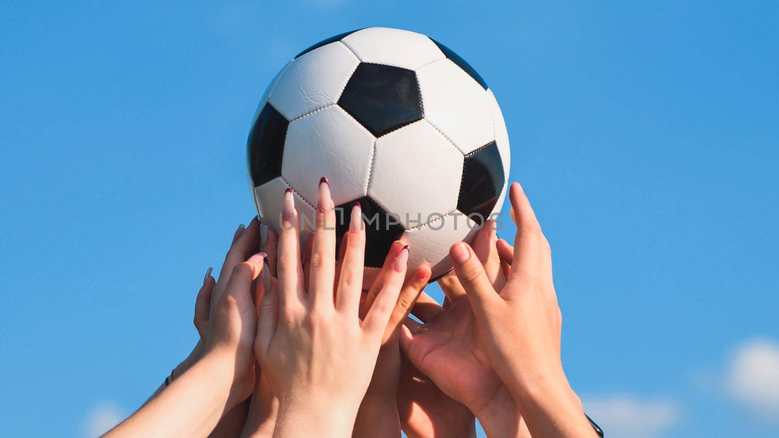 Group of hands holding a soccer ball under a clear blue sky, representing unity, camaraderie, and fair play in educational settings