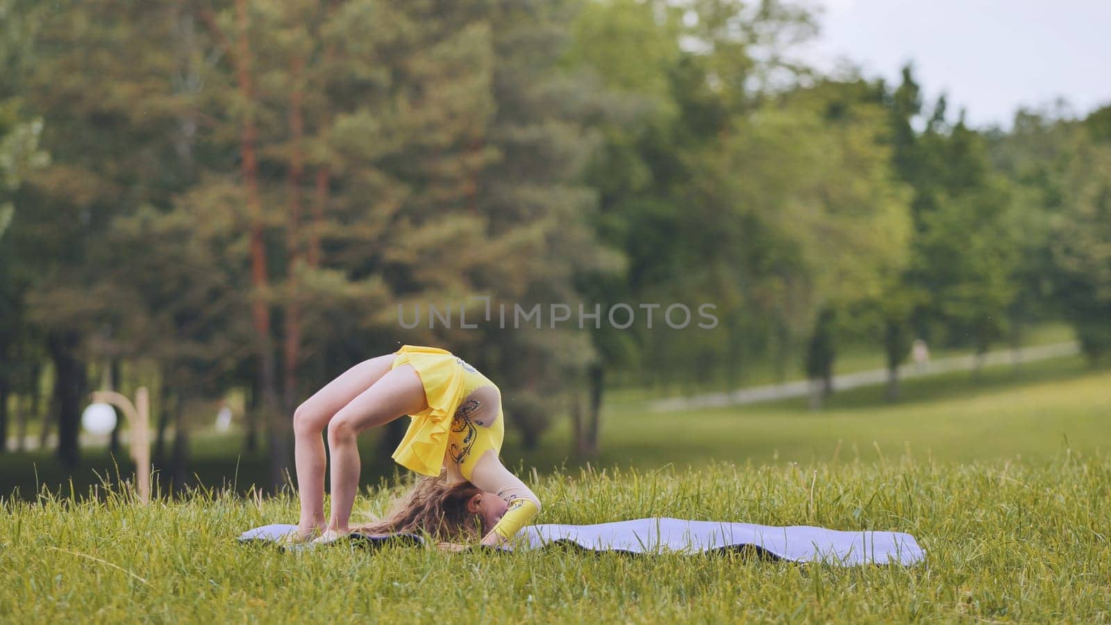 Flexible girl practicing gymnastic backbend exercise on a mat in a park, showing dedication to training and healthy lifestyle