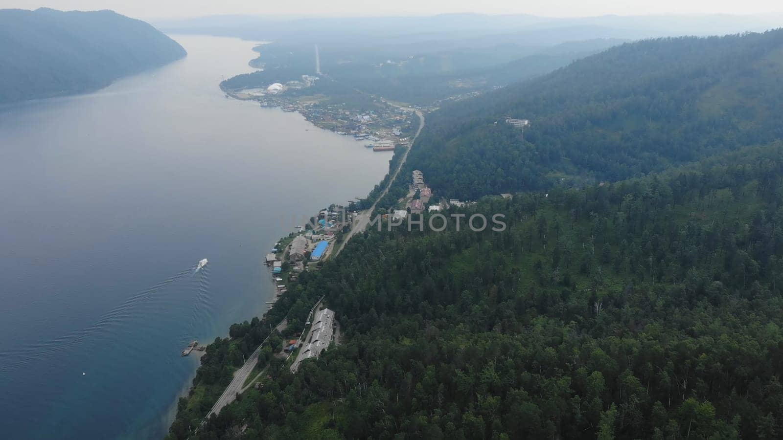 Aerial view of lake teletskoye with a motorboat sailing along the shore near artybash village, surrounded by the altai mountains