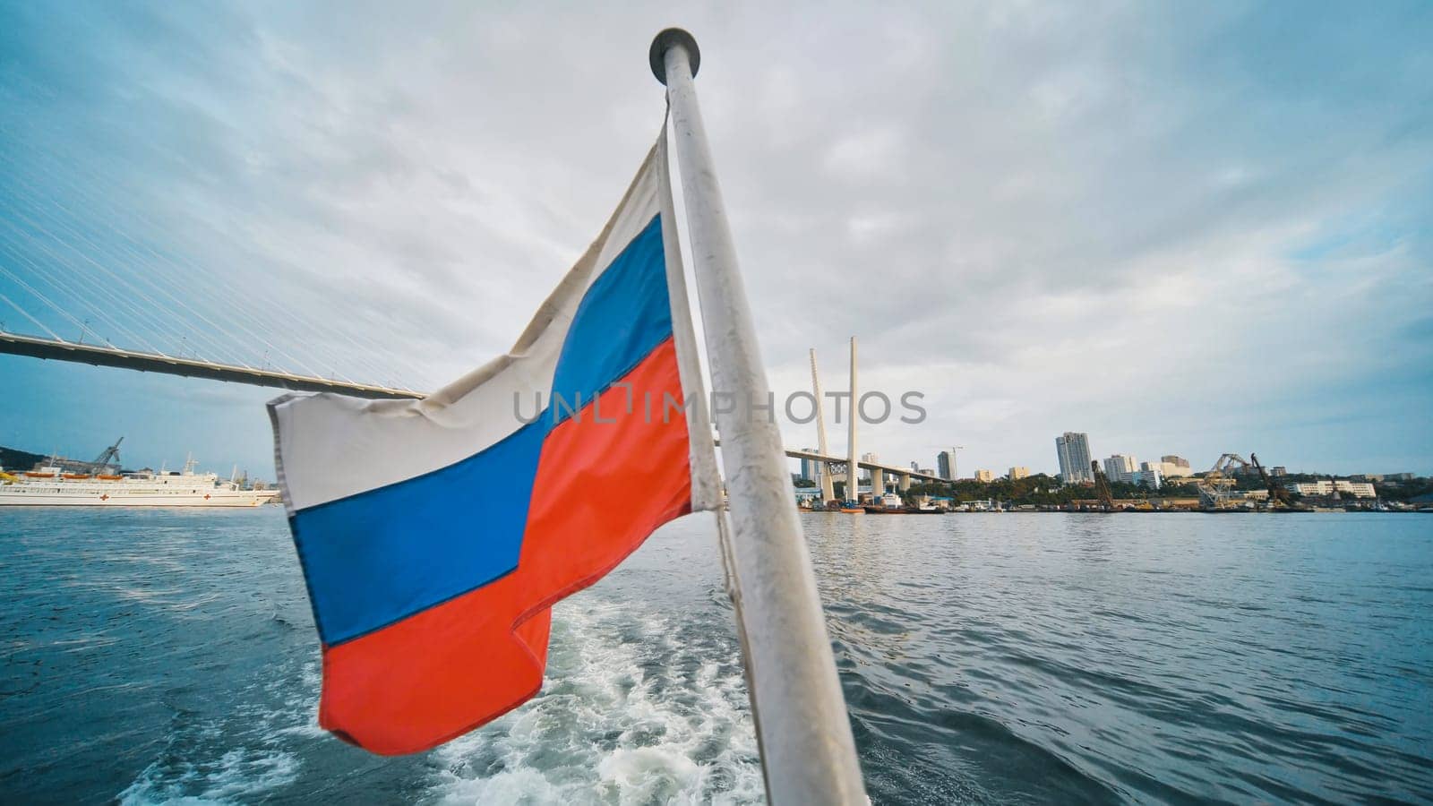 Russian national flag flying from vessel navigating eastern golden horn bay near zolotoy rog bridge in vladivostok waterfront