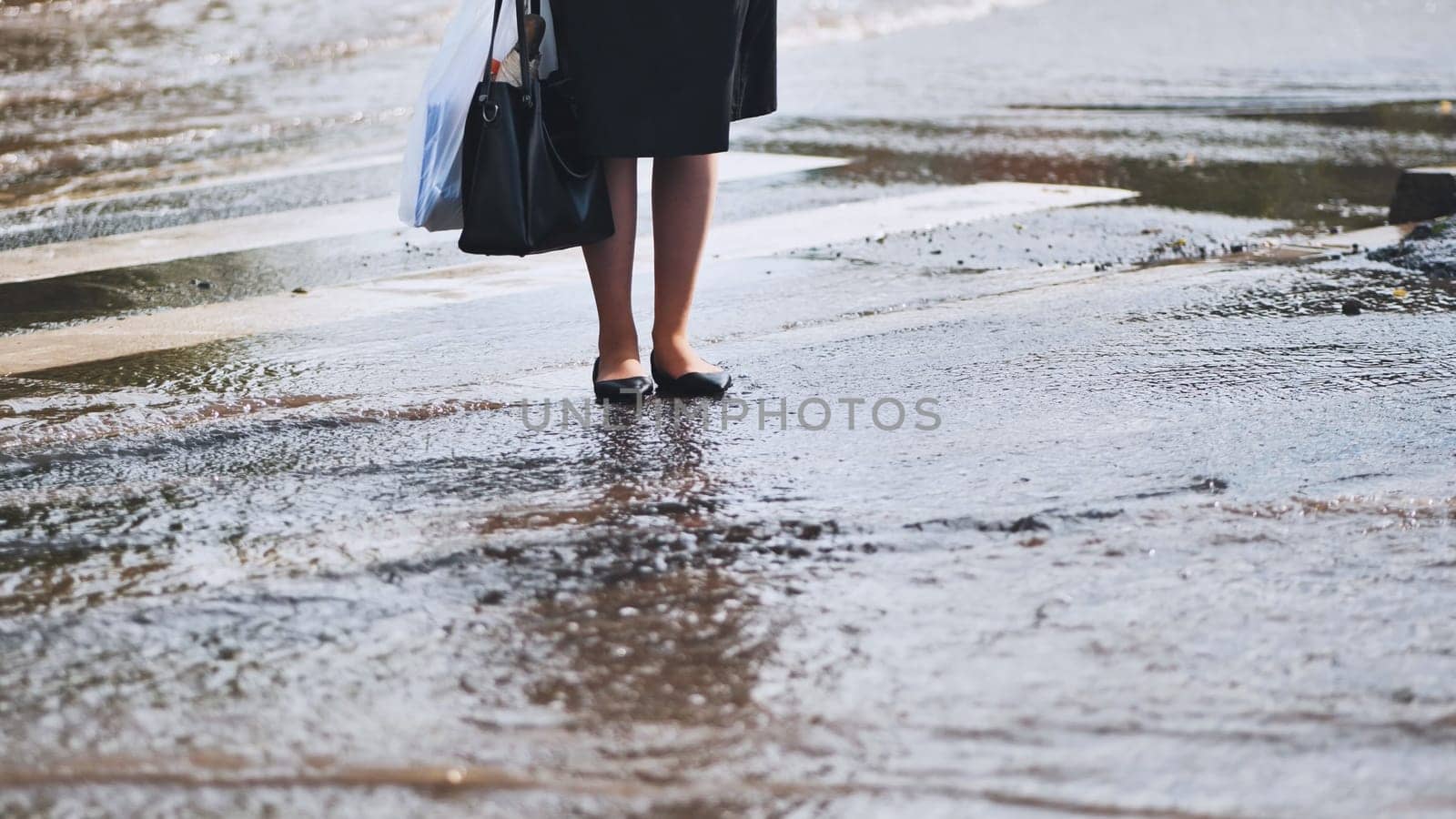 Professional woman navigating flooded urban street, carrying shopping and handbag during rainfall aftermath