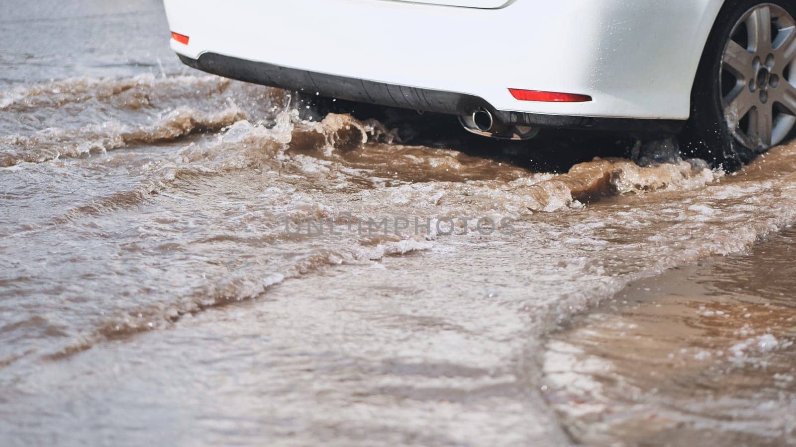 White car making waves driving through flooded street after heavy rain, creating a splash