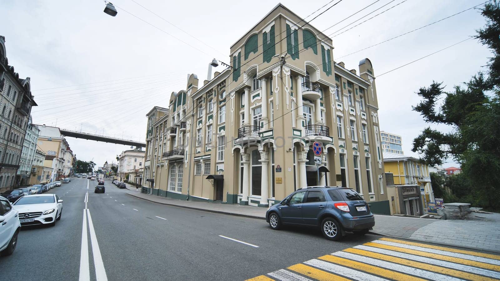 Ornate art nouveau building with green and beige facade located on a street in vladivostok, russia, featuring a pedestrian crossing and parked cars