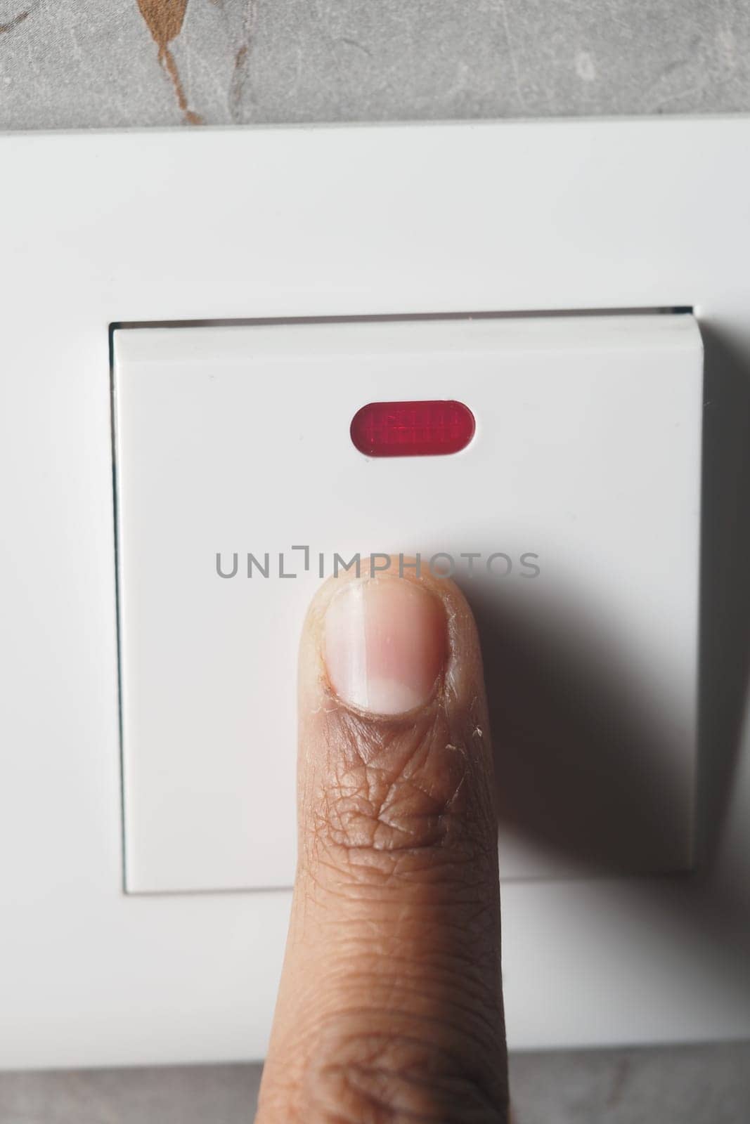 A finger presses a light switch, signaling an intention to turn on or off a light. This simple action demonstrates everyday life in a modern home environment.