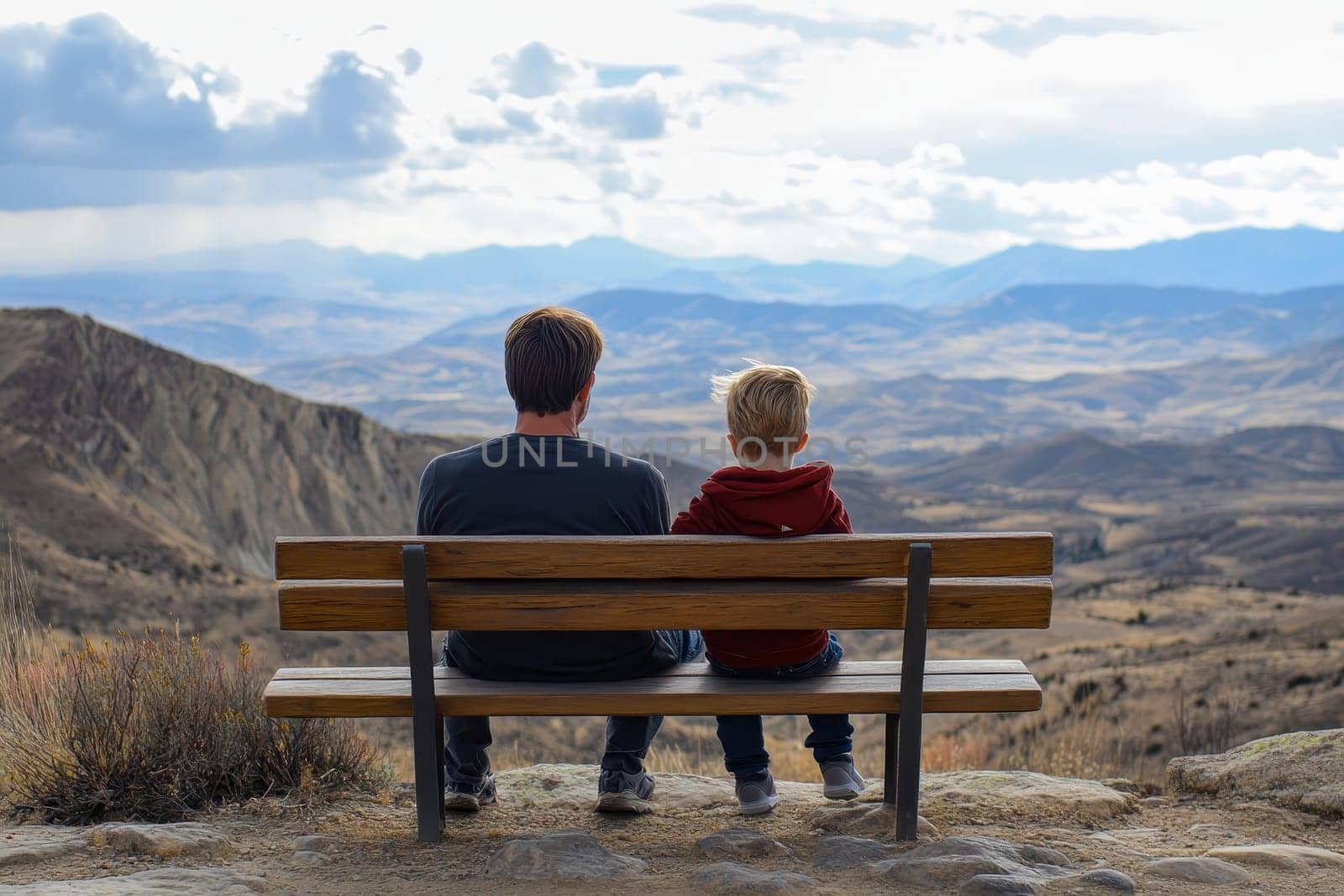 A father and son sit side by side on a wooden bench, gazing over a stunning mountain landscape under a dramatic sky.