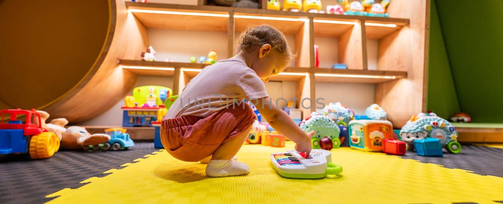 Toddler playing with colorful musical toy piano in a bright playroom filled with educational toys and activities for early childhood development