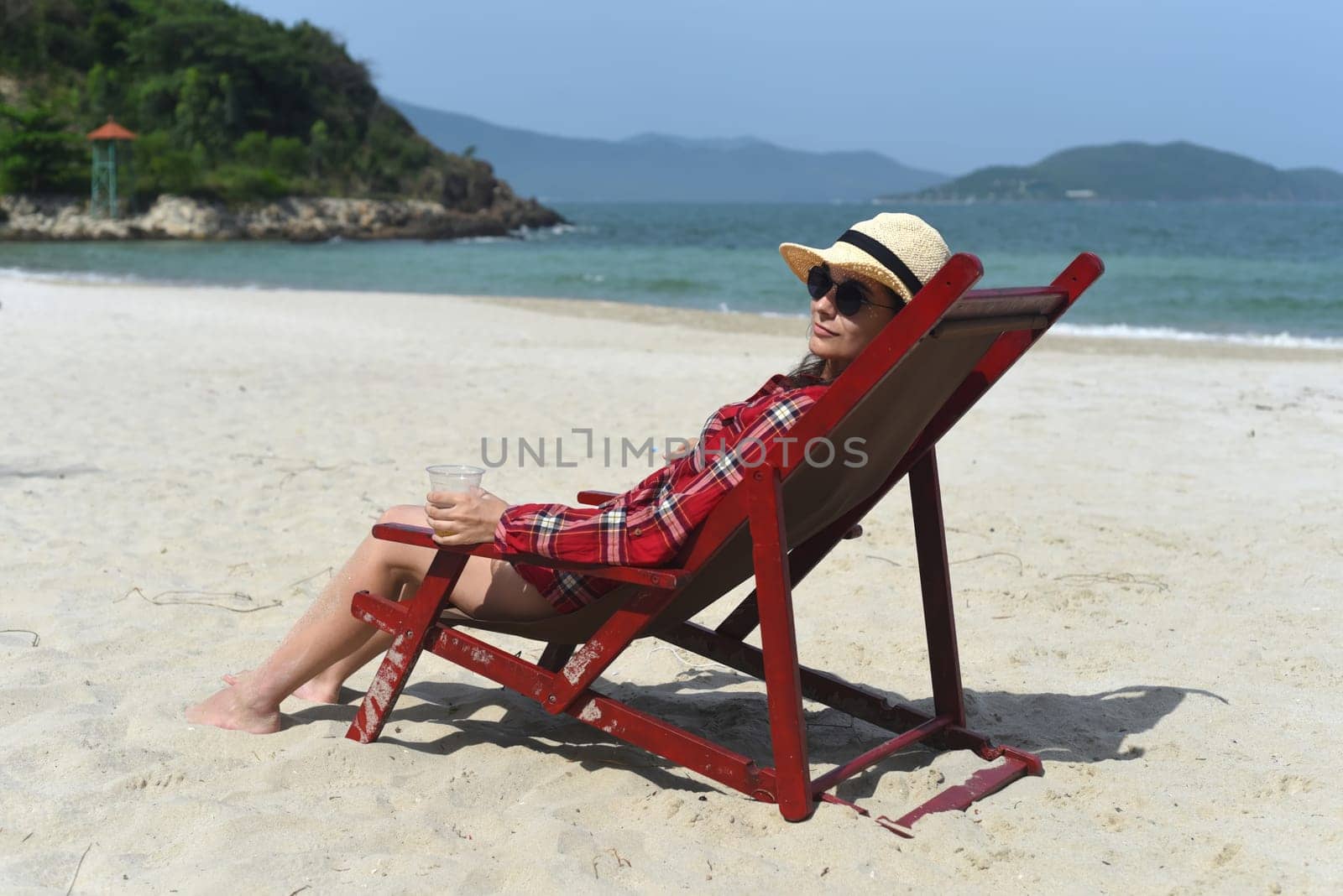 Young woman in hat sitting on the desk chair at the beach with white sand in Vietnam