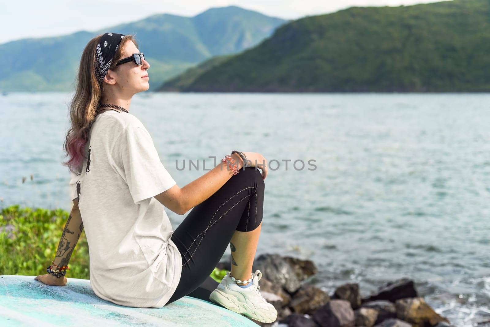 Young travel woman sitting with sunglasses and bandana on the shore of south china sea in vietnam