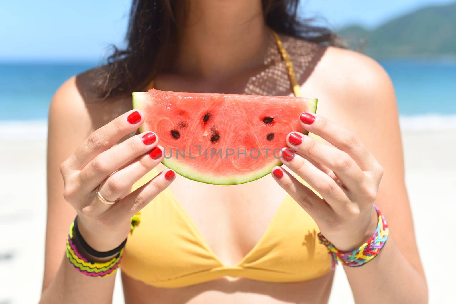 Young woman in swimsuit eats watermelon against south china sea in Vietnam