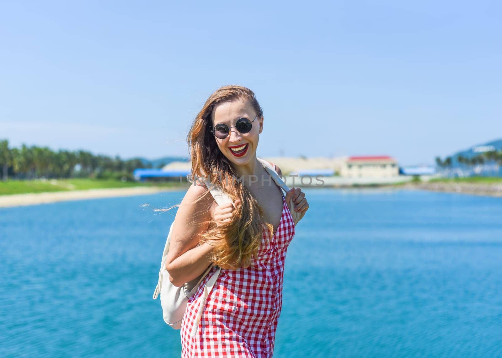 Bright blond young woman standing with backpack near sea in summer