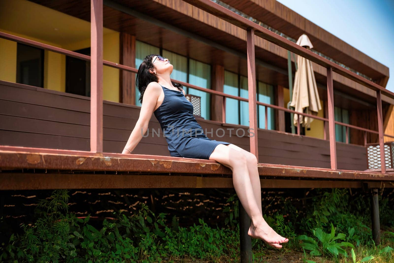 50 years old russian woman in short dress and sunglasses sitting on a balcony and enjoying on the summer day