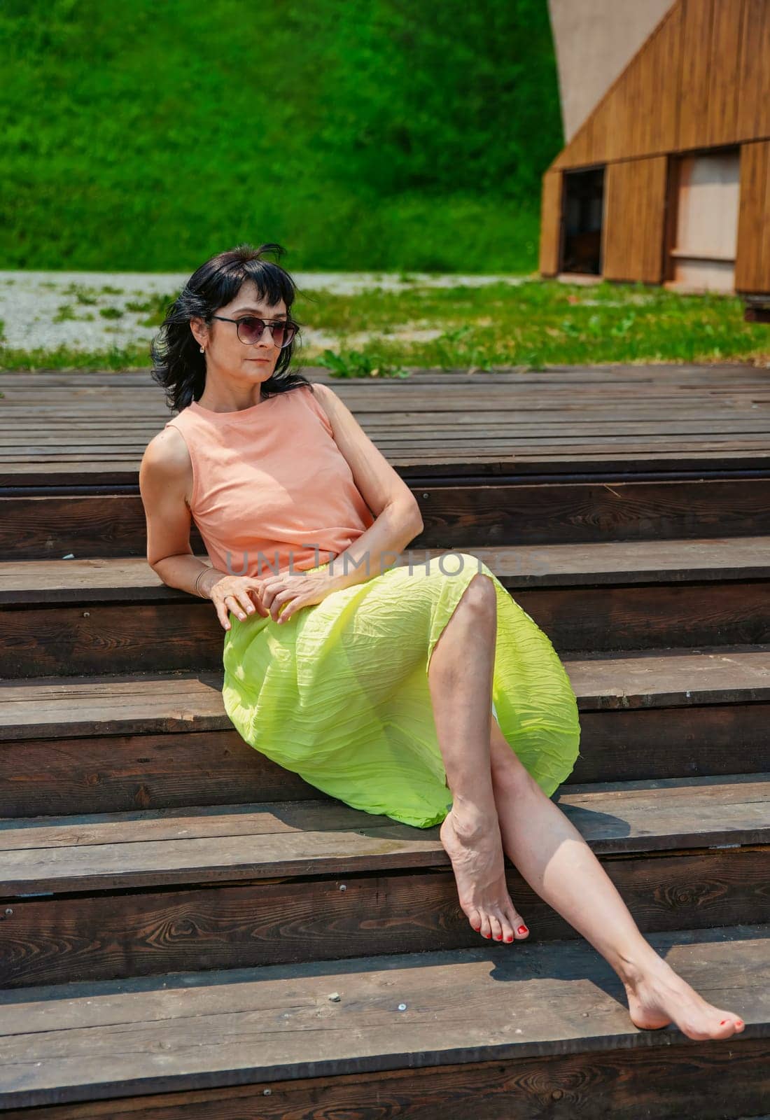 50 years old russian woman in short dress and sunglasses sitting on a stairs and enjoying on the summer day