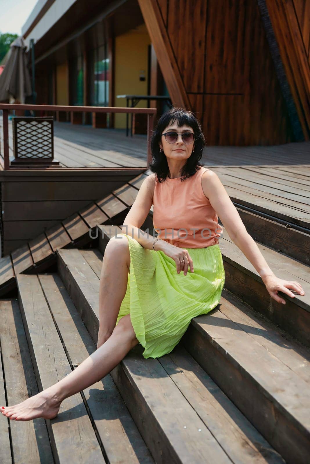 50 years old russian woman in short dress and sunglasses sitting on a stairs and enjoying on the summer day