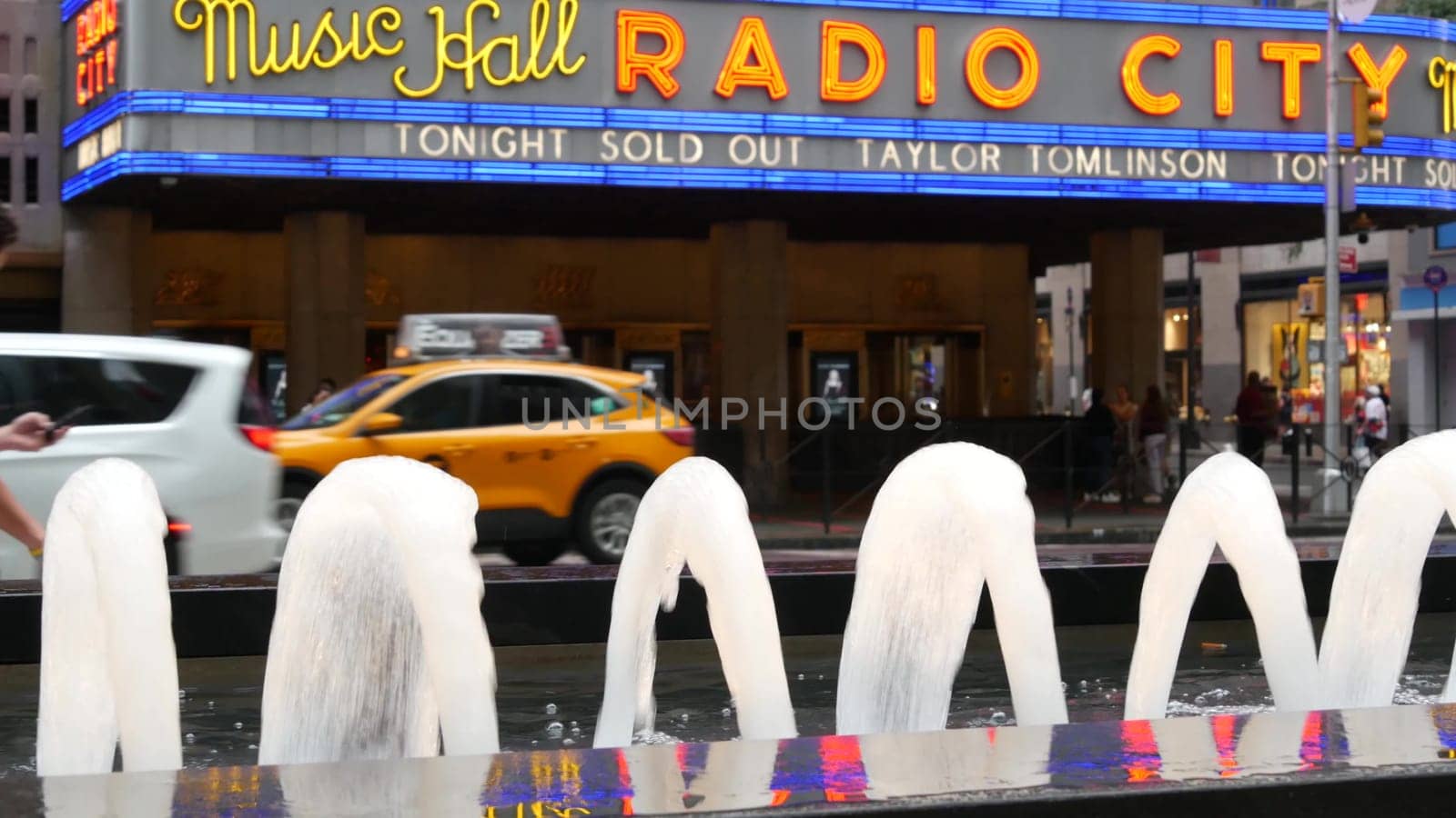 New York, United States - 10 Sept 2023: Manhattan Midtown street. Radio City Music Hall, Rockefeller Center, USA. People pedestrian, urban traffic, 6 Sixth Americas avenue crossroad, yellow taxi cab.