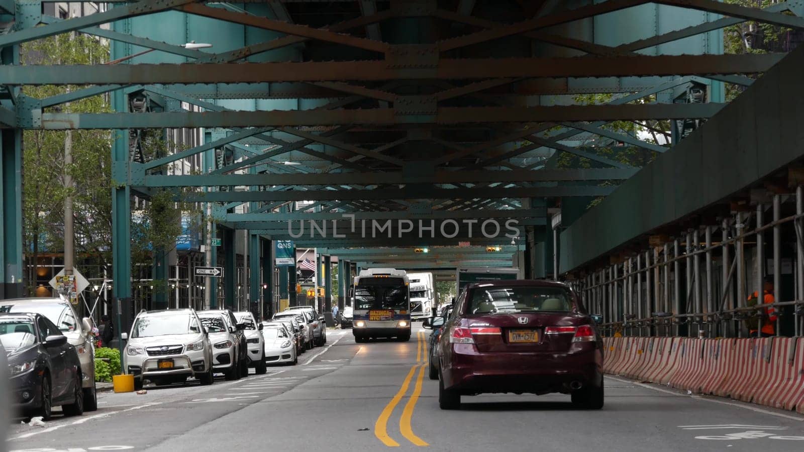 New York City, United States - 31 Aug 2023: Elevated subway above street. Metropolitan bridge over road, Queens. Long Island metro line, Court Square. Cars and bus under railway track. NYC urban life.