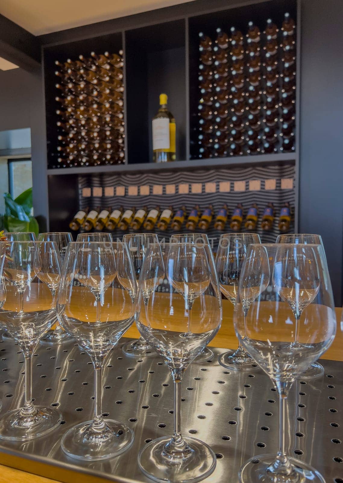 A row of sparkling wine glasses is positioned in front of a beautifully designed wine rack holding bottles of Sauternes. The setting is warm and inviting, perfect for wine tasting.