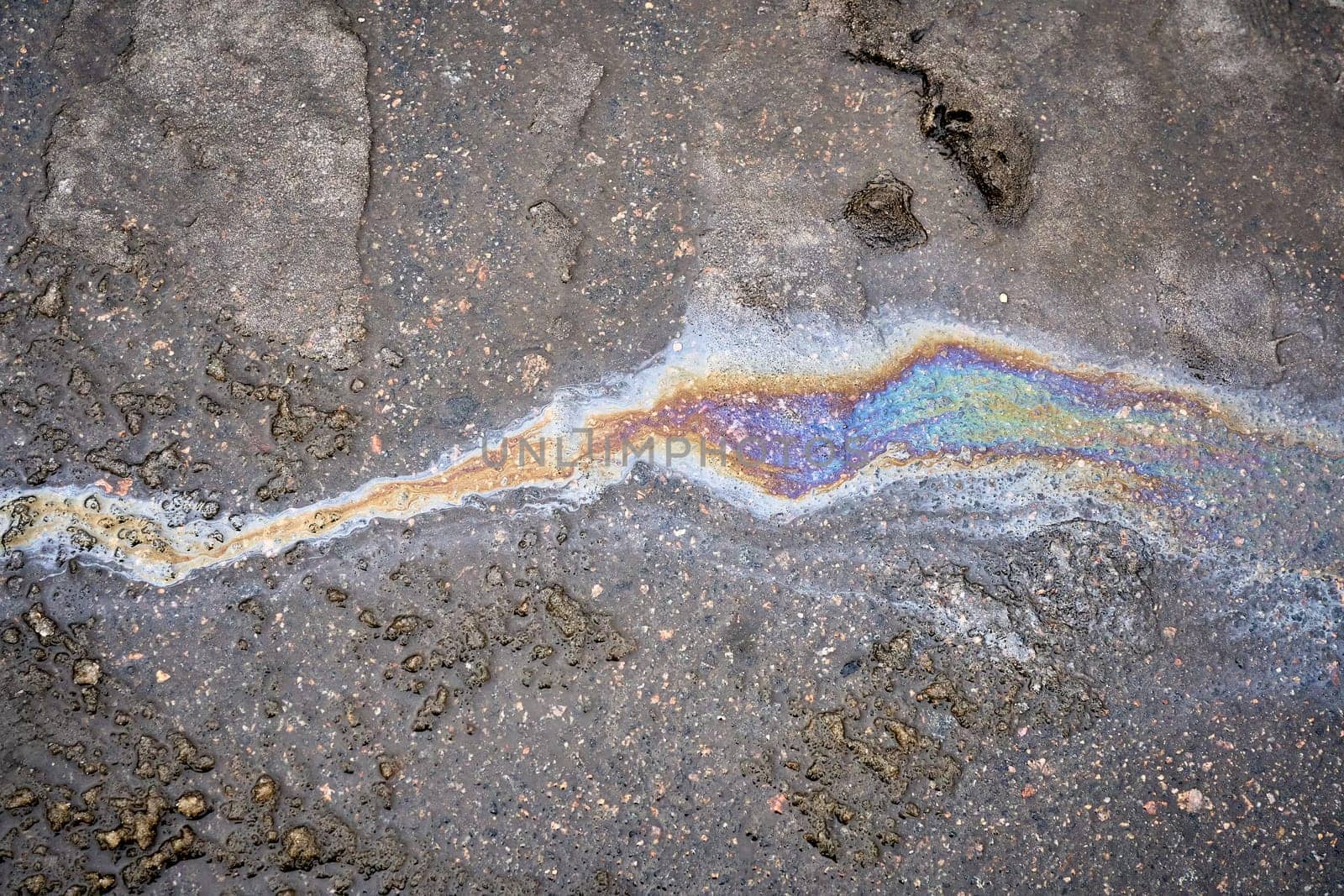 Brilliant oil leak creating a vibrant rainbow sheen on the surface of a wet road.