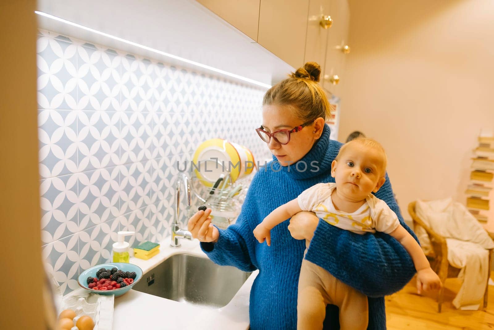 A loving mother gently cradles her baby in her arms, all while she prepares delicious food in a modern kitchen