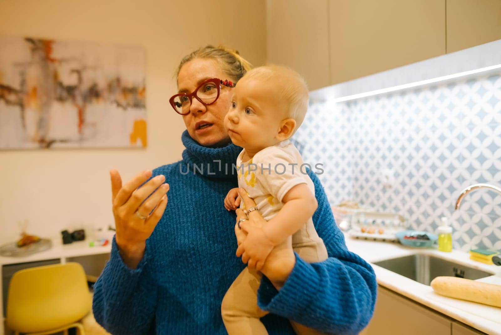 A loving mother holds her adorable baby while having a warm conversation in a stylish, contemporary kitchen environment