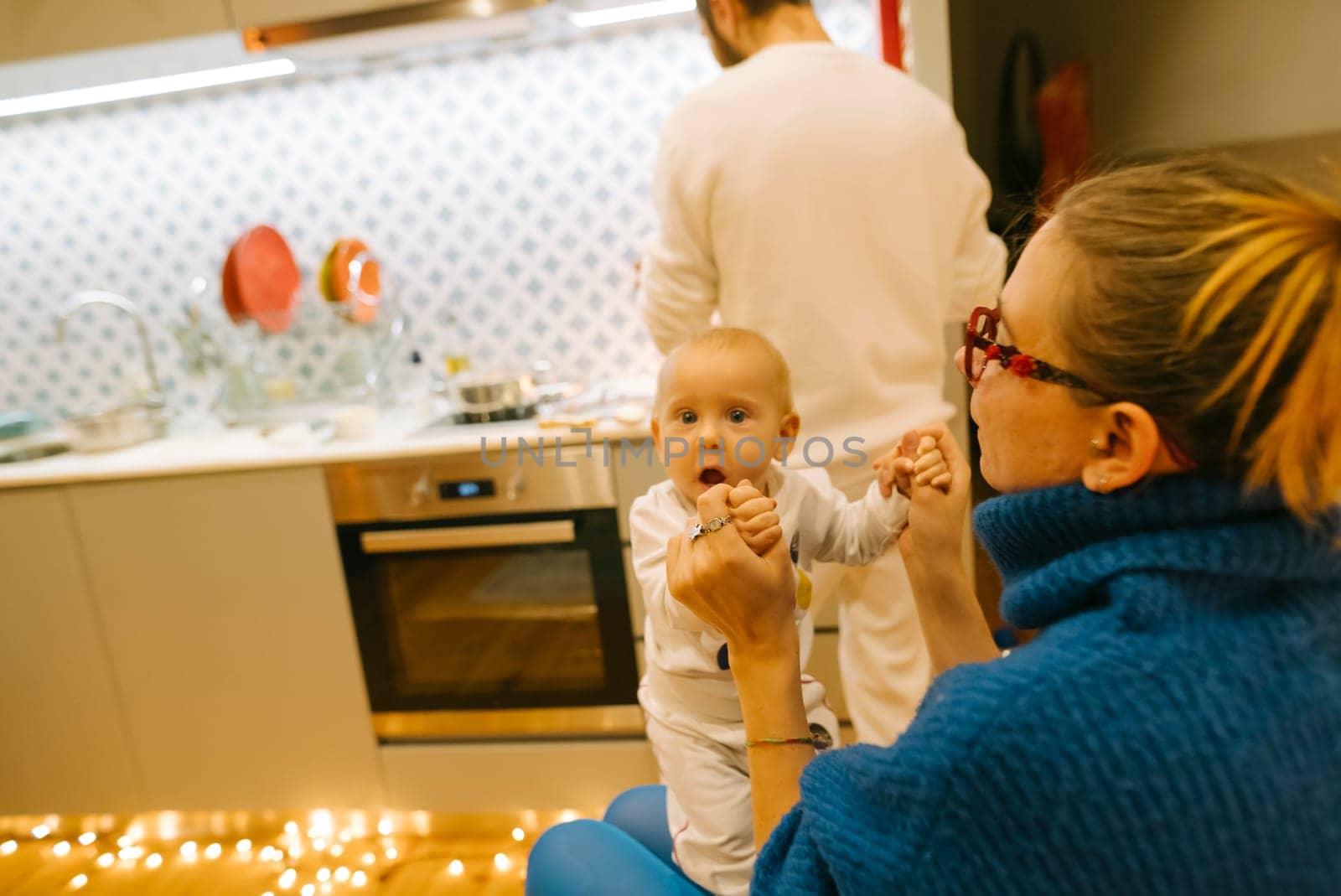 A heartwarming scene of a cute baby practicing walking with family members in a lovely modern kitchen