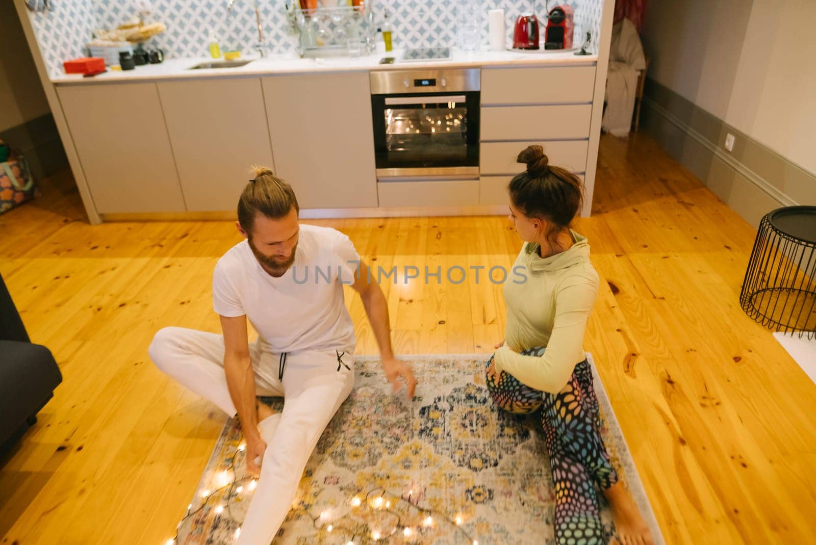 A couple engaged in practicing various yoga poses together on a soft rug in a stylishly designed kitchen setting