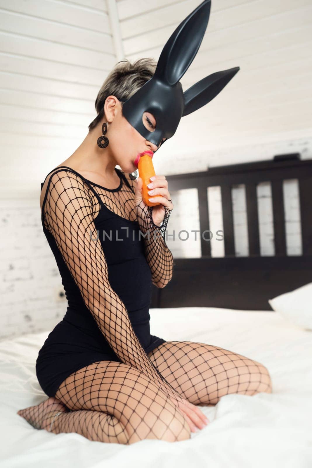 A sexy girl in a short black dress and a rabbit mask from sex shop erotically plays with carrots on her hand and in her mouth, nibbling