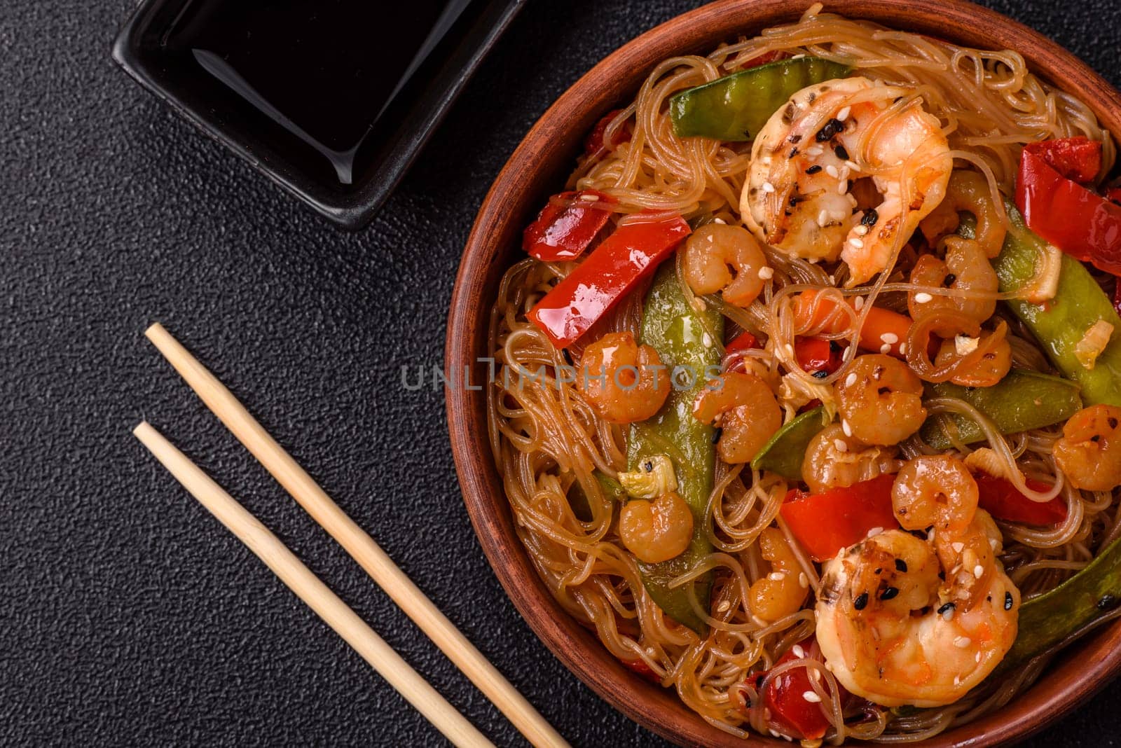 Glass noodles with shrimps and seafood, vegetables, spices and soy sauce on dark concrete background