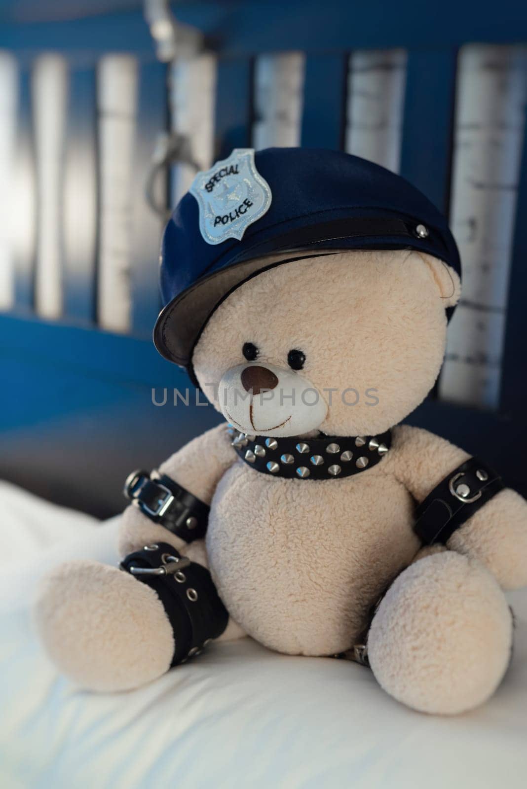 A toy teddy bear dressed in leather straps is a BDSM accessory for adult games in a police hat on the bed