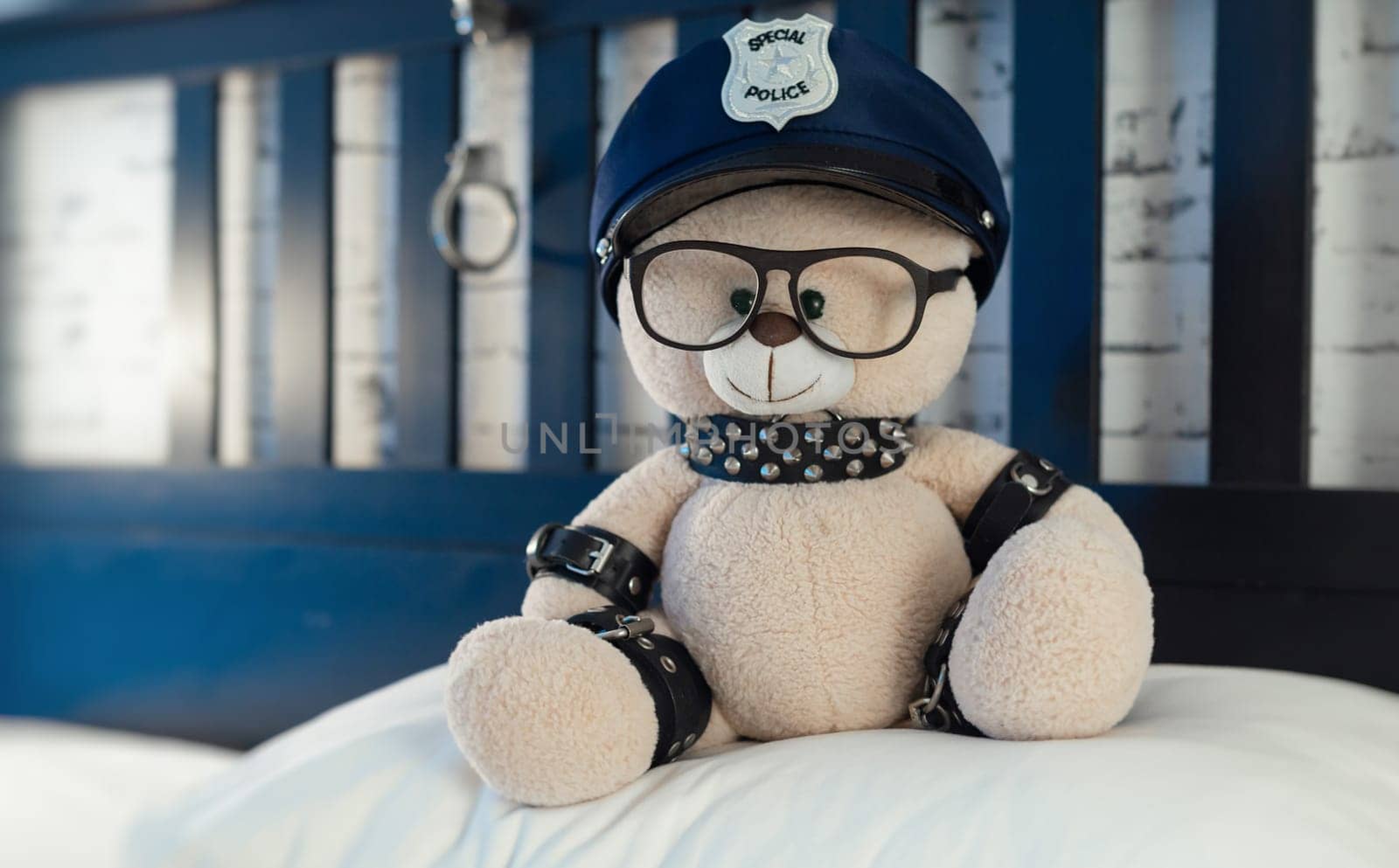 A toy teddy bear dressed in leather straps is a BDSM accessory for adult games in a police hat on the bed