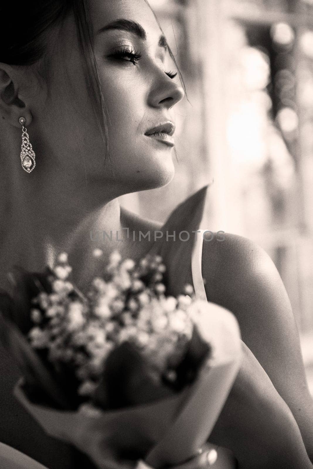 A close up of a woman. High quality photo. close-up of a brunette girl, she has her hair beautifully styled. She holds a bouquet of lilies of the valley in her hands. Black and white photo