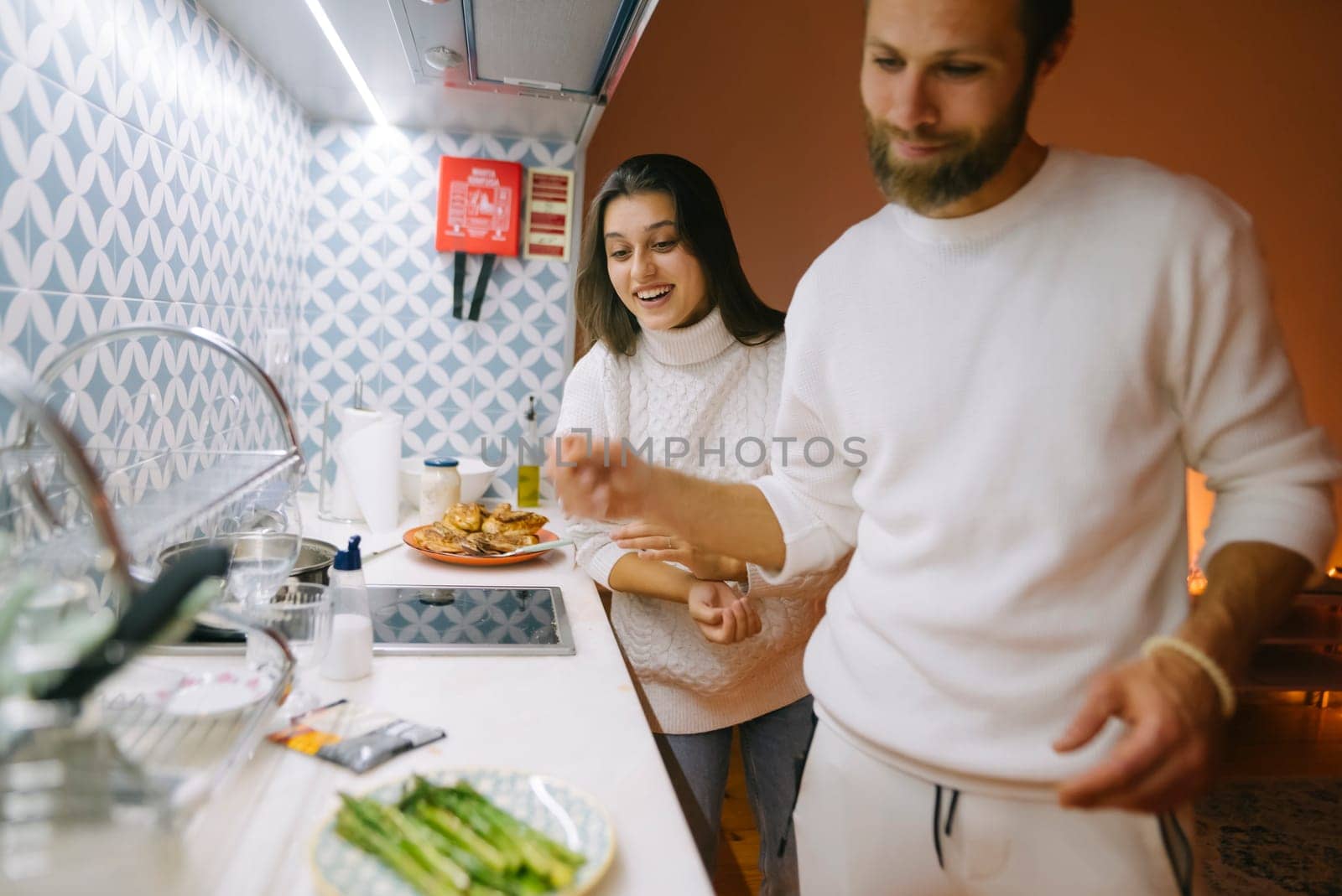 A joyful couple is happily preparing a delicious meal together in a modern, stylish kitchen at their home