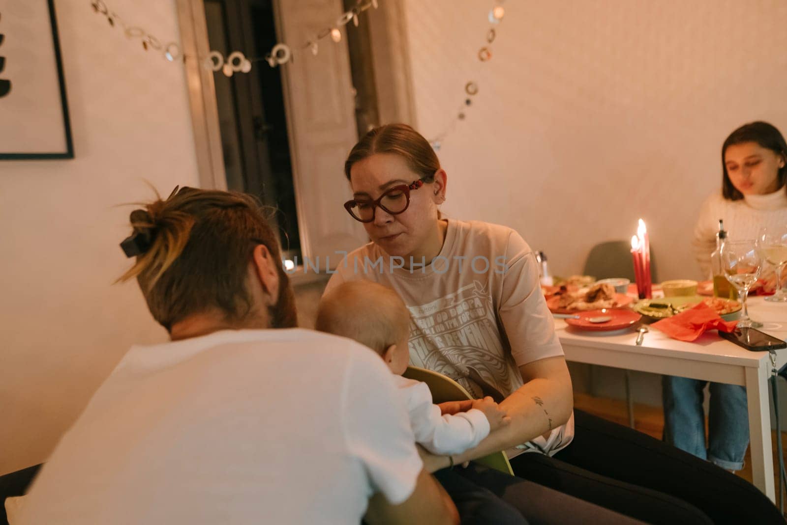 A cozy and warm family gathering filled with a baby, flickering candles, and an enchanting festive table setting